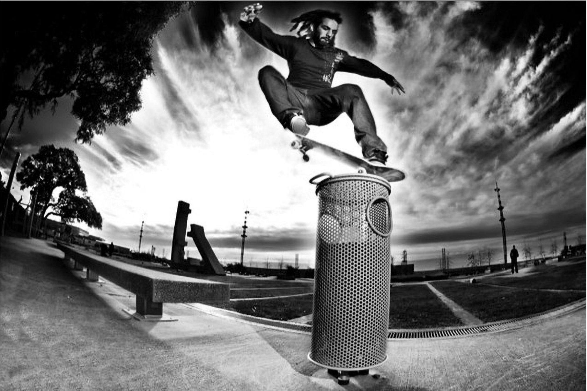 Skater saltando sobre un basurero metálico, foto en blanco y negro con cielo dramático